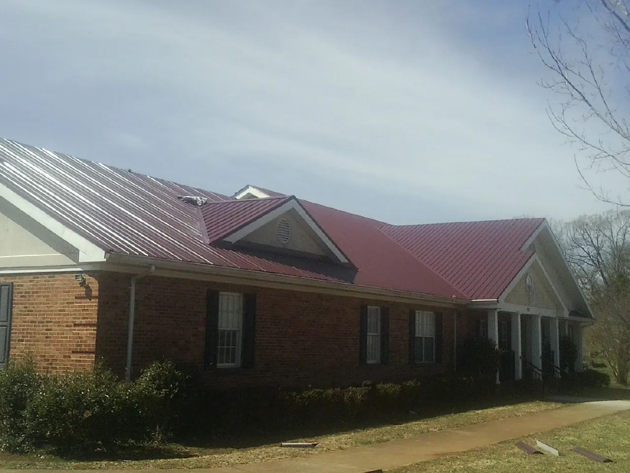 Red metal roof with gabled entries on a long brick building, from a Hail Damage Roof Repair job in Northern Cambria