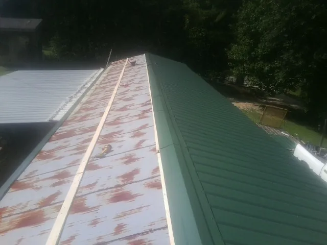 Old rusted panels beside newly installed green metal roofing — Wind Damage Roof Repair by Roofing Brothers in Northern Cambria