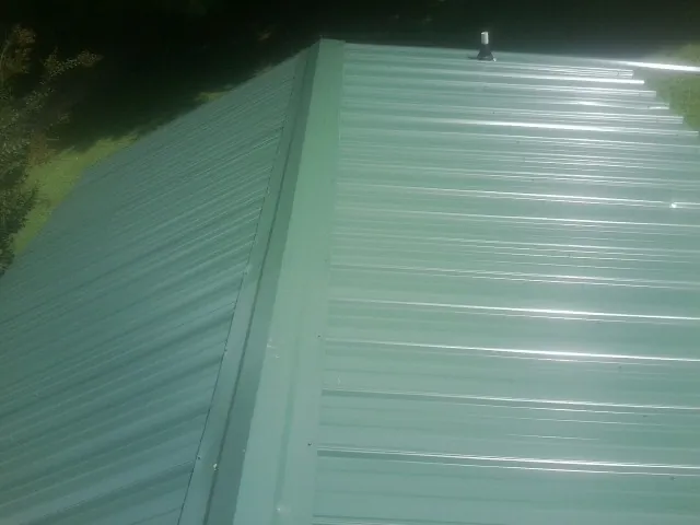 New green metal panels meeting at the ridge of a roof — Flat Roof Repair work by our crew in Northern Cambria