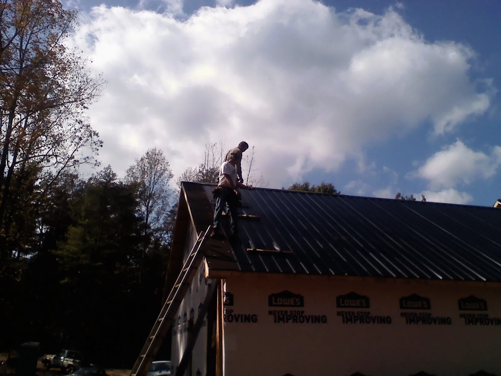 Roofer fastening dark metal panels high against a cloudy sky, from a Roof Inspection job in Northern Cambria
