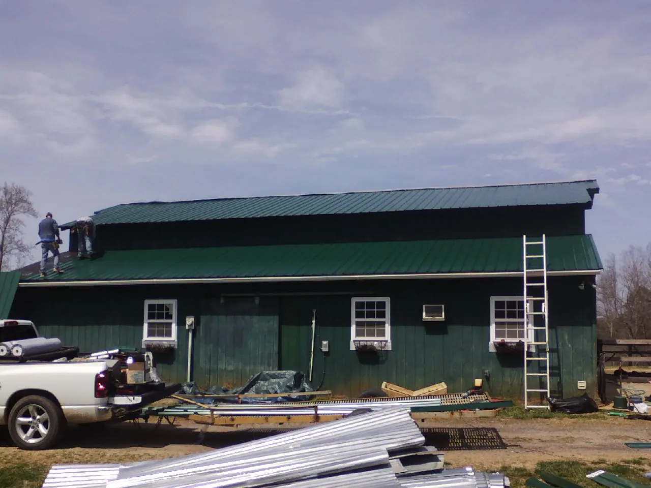 Crew installing green metal roofing on a large green barn in Northern Cambria