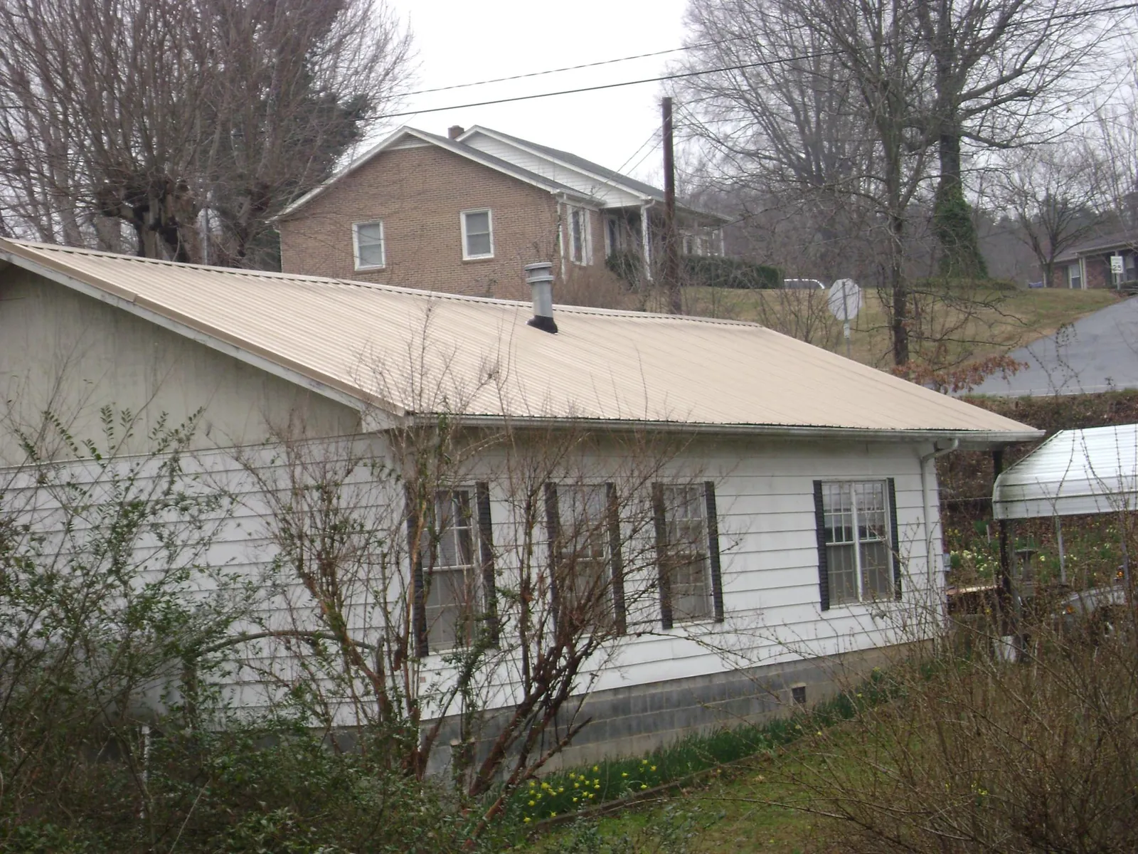 Tan metal roof on a white sided house set into a hillside — Commercial Roofing by Roofing Brothers in Northern Cambria