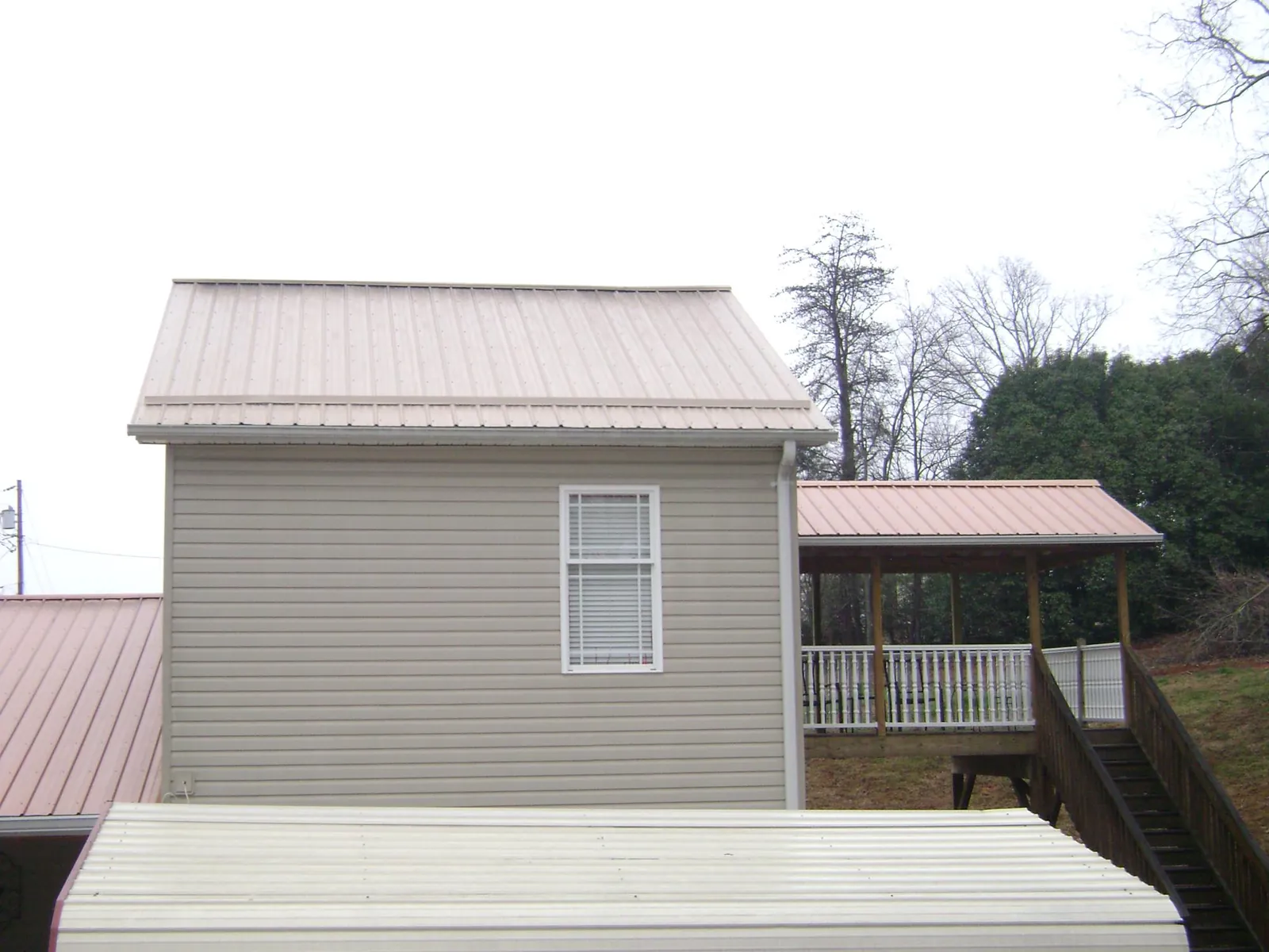 Tan metal roofs on a two story addition and attached porch, from a Roof Replacement job in Northern Cambria